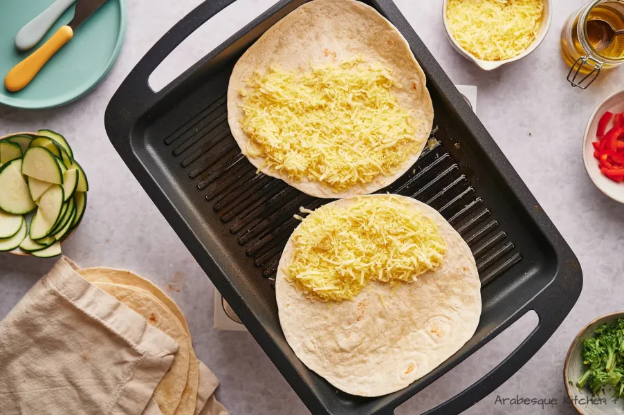 Placer 2 feuilles de tortillas sur le gril et recouvrir la moitié de chacune avec le fromage cheddar.