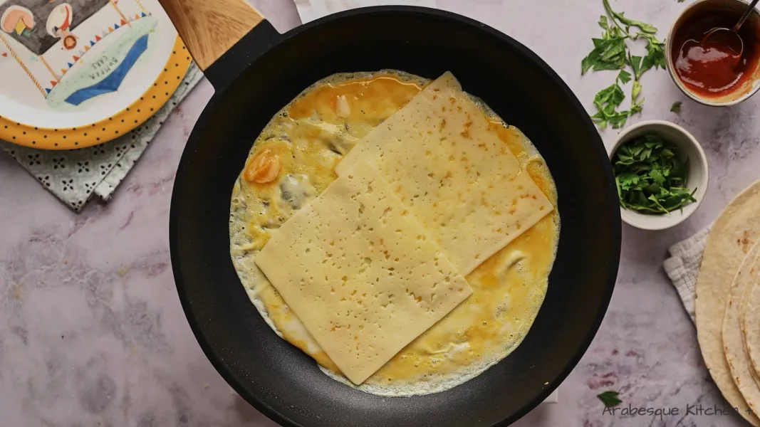 Laisser les œufs se répartir sur toute la surface. Garnir de deux tranches de fromage et laisser cuire environ une minute.