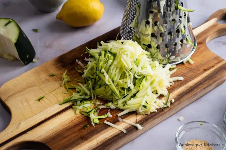 Shred the zucchini using the large side of the grating box. Transfer to a fine mesh strainer and press it down with the back of a spoon to remove as much water as possible.
