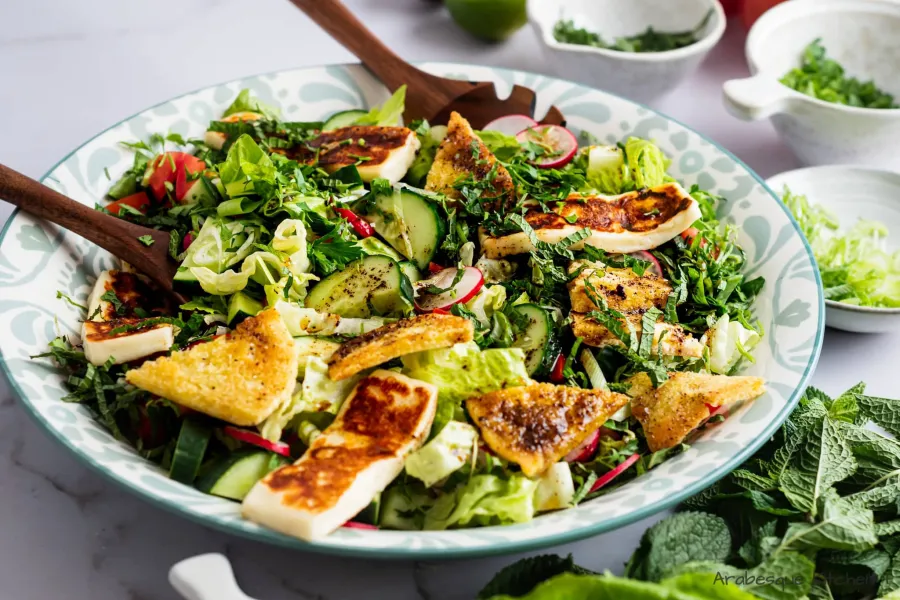 Serve the salad by layering the veggies, topping with green onions, fresh herbs, halloumi slices, pita breads and the dressing.
