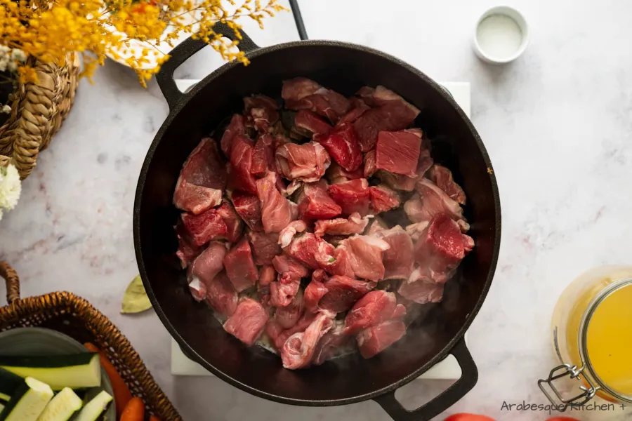 نسخن الفرن الهولندي على درجة حرارة متوسطة إلى عالية ونضيف الزبدة وقطع لحم الضأن. نعملها على دفعات حتى يتحول لون اللحم إلى اللون البني من كل جانب.